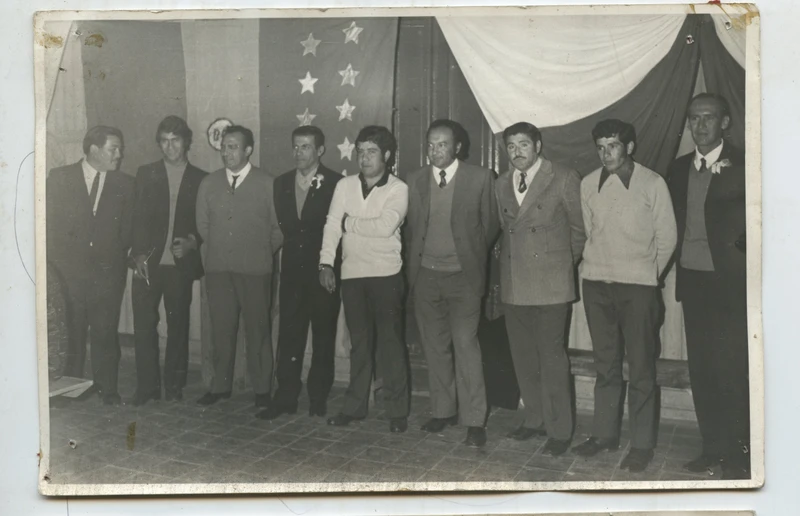Grupo de hombres posando frente a bandera